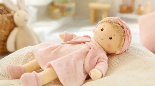 Niedliche Spielzeug-Babypuppe mit weichem Stoffkörper und freundlichem Gesicht auf einer hellen Strickdecke im Kinderzimmer