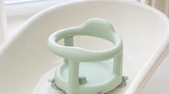 Baby-Badewannensitz aus hellgrünem Kunststoff mit Sicherheitsringen und Saugnäpfen in einer hellen Babybadewanne