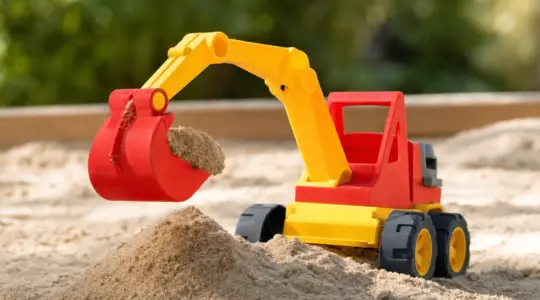 Ein robuster Spielzeug-Bagger in fröhlichen Farben mit beweglicher Schaufel in einem Sandkasten mit etwas aufgehäuftem Sand