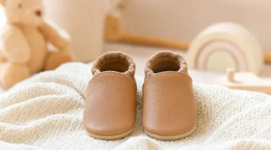 Ein Paar weiche Krabbelschuhe aus zartem Leder für Babys steht ordentlich nebeneinander auf einer hellen Decke