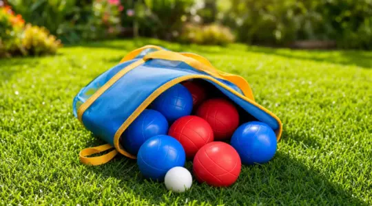 Ein buntes Boccia-Set mit weichen Kugeln liegt in seiner Tasche auf einer sonnigen Wiese im Garten