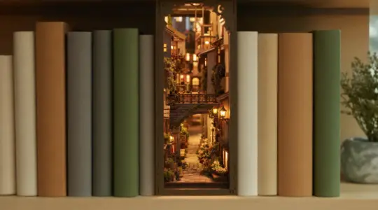 Ein beleuchteter Book-Nook-Bausatz als Miniatur-Gasse steht detailreich zusammengebaut zwischen Büchern in einem Regal
