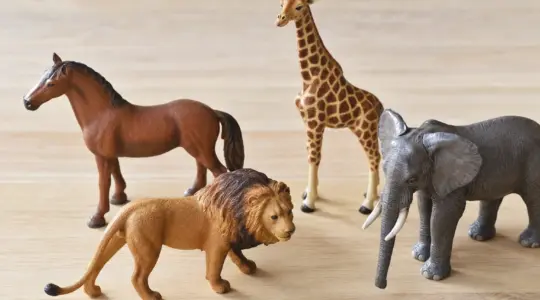 Mehrere realistisch gestaltete Spielzeug-Tierfiguren mit Löwe, Elefant und Giraffe auf Holzfläche