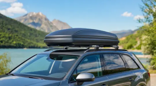 Eine stromlinienförmige, geschlossene Dachbox ist sauber auf dem Dachträger eines Autos montiert, bereit für den Familienurlaub