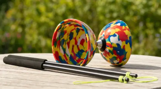 Ein buntes Diabolo mit zwei Handstäben und einer Schnur liegt auf einer Holzfläche im Freien