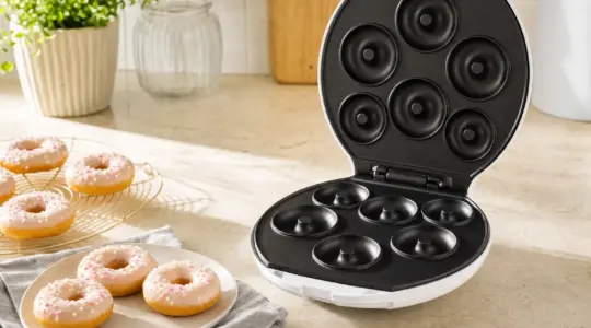Ein elektrischer Donut-Maker mit fertigen Donuts auf einer hellen Küchenarbeitsplatte