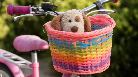Ein bunter kindgerechter Fahrradkorb aus Geflecht ist am Lenker eines Kinderfahrrads befestigt
