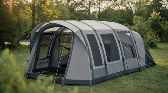 Ein großes modernes Familienzelt in Grau und Anthrazit aufgebaut auf einer grünen Wiese auf einem ruhigen Campingplatz mit Bäumen im Hintergrund