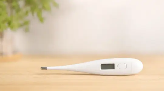 Modernes digitales Kinder-Fieberthermometer aus weißem Kunststoff mit ausgeschaltetem Display auf einem hellen Holztisch