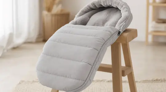 Kuscheliger gefütterter Fußsack für den Kinderwagen in warmem Hellgrau mit Plüschfutter und Reißverschluss auf einem hellen Holzhocker