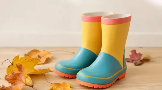 Paar bunte Kinder-Gummistiefel nebeneinander auf einem hellen Holzboden mit Herbstblättern