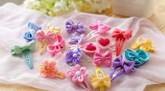 Fröhliches Set bunter Kinder-Haarspangen und Haarclips mit Schleifen, Herzen und Blüten auf einem hellen Holztisch