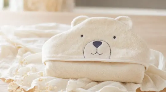 Flauschiges weiches Baby-Kapuzenhandtuch in zartem Creme mit niedlicher Bären-Kapuze, gefaltet auf einem hellen Holztisch
