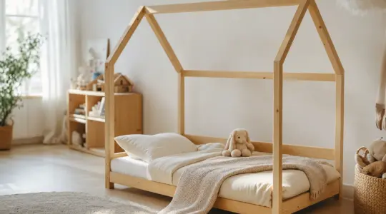 Gemütliches Kinderbett aus hellem Holz in Hausbett-Form mit weißer Matratze und heller Bettwäsche in einem freundlichen Kinderzimmer
