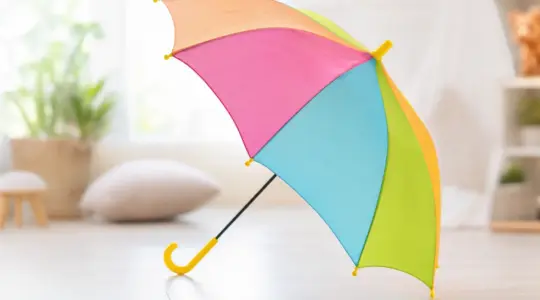 Ein aufgespannter bunter Kinderregenschirm in fröhlichen Farben mit kindgerechtem Bogengriff freistehend vor einem hellen, freundlichen Hintergrund