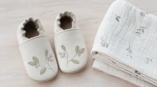 Ein Paar weiche Baby-Krabbelschuhe aus hellem Leder liegt nebeneinander auf einer Holzfläche