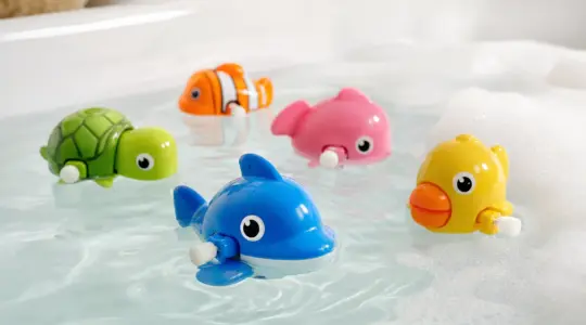Bunte aufziehbare Schwimmtiere als Badespielzeug schwimmen in einer mit Wasser gefüllten Wanne neben fröhlichem Schaum