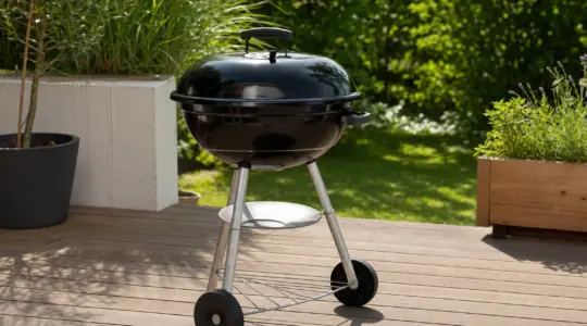 Ein schwarzer Kugelgrill steht auf einer sonnigen Terrasse im Garten