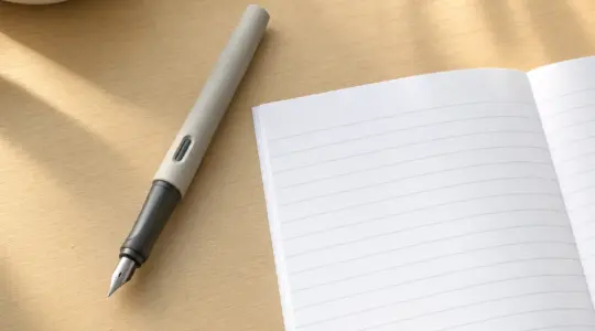 Ein moderner Schulfüller mit ergonomischer Griffzone liegt zusammen mit einem Schreibheft auf einem hellen Tisch