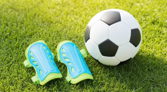 Ein Paar Kinder-Schienbeinschoner für Fußball auf einer Rasenfläche neben einem Ball