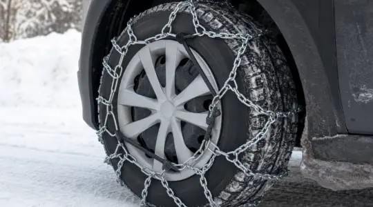 Montierte Schneeketten aus Metall liegen auf dem Reifen eines Autos im Schnee
