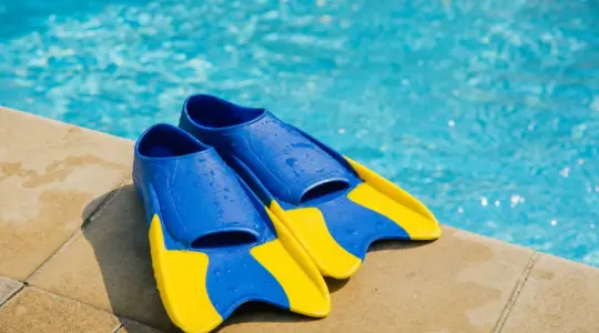 Ein Paar bunte Kinder-Schwimmflossen liegt am Rand eines Pools auf hellen Fliesen