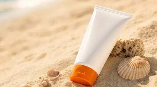 Neutrale Sonnencreme-Tube für Kinder mit orangefarbenem Deckel auf hellem Sand am Strand