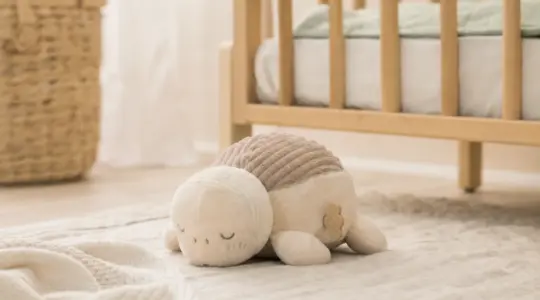 Niedliche Baby-Spieluhr als weiches Stofftier in zarten Naturtönen auf einer hellen Krabbeldecke neben einem Babybett