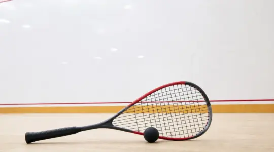 Ein Squashschläger liegt mit einem Squashball auf dem Boden eines Courts
