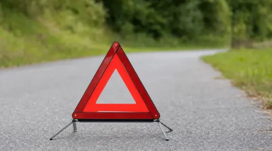 Ein rotes reflektierendes Warndreieck steht aufgeklappt auf einer Straße