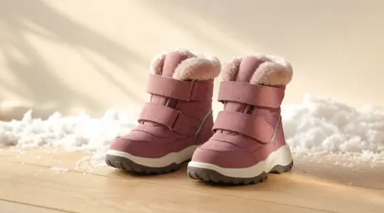Paar warm gefütterte Kinder-Winterstiefel mit Profilsohle und Klettverschluss nebeneinander auf hellem Boden mit Schnee