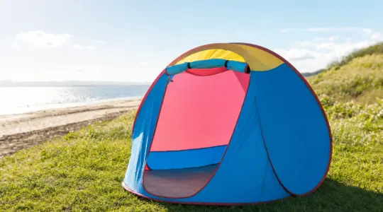 Ein aufgestelltes buntes Pop-up-Wurfzelt auf einer grünen Wiese am Rande eines Strandes