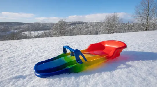 Ein bunter Zipfelbob aus Kunststoff auf einer verschneiten Wiese in der Wintersonne